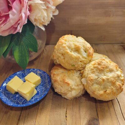 four cheese and onion scones sitting on a wooden board with butter on the side