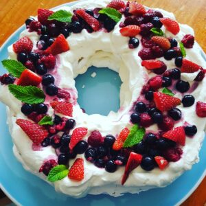 a wreath pavlova sitting on a blue plate with fresh mixed berries on top