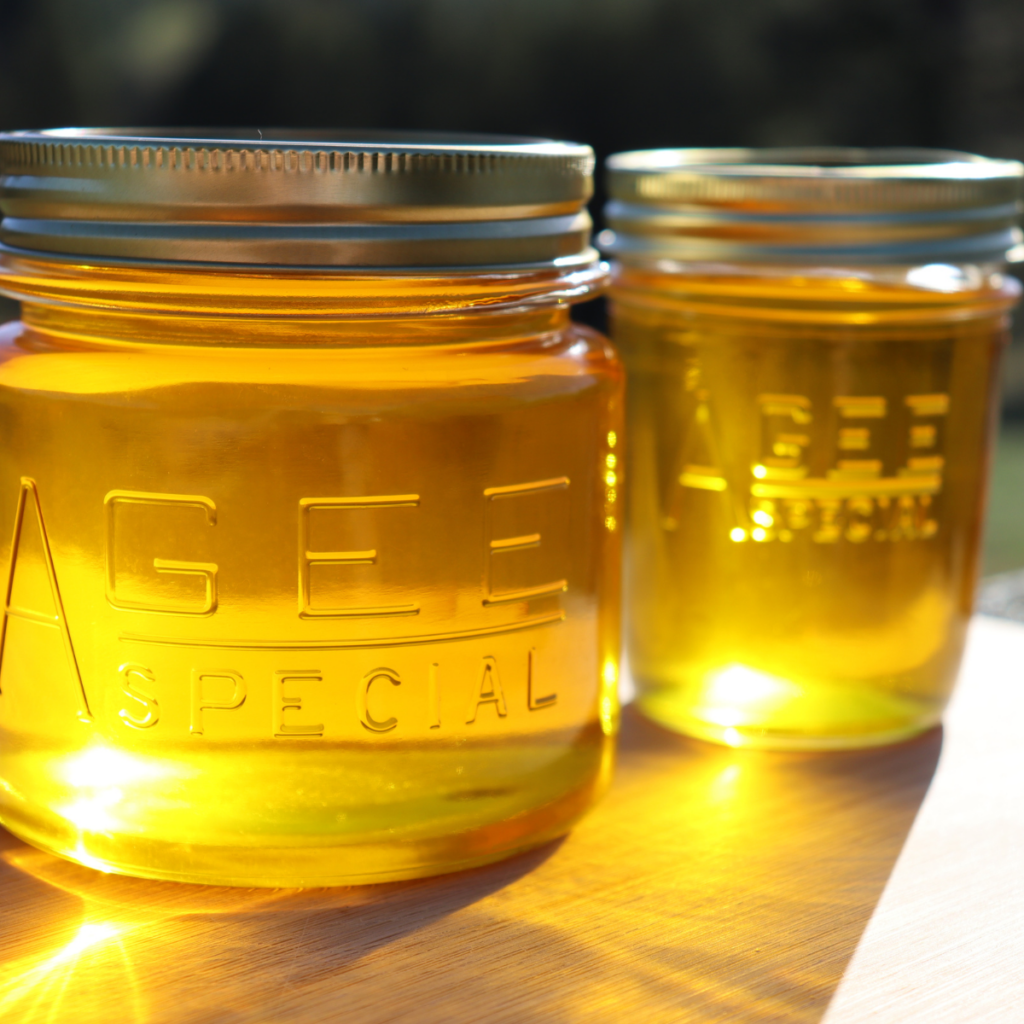 two glass jars of yellow ghee on a wooden board with the sunlight showing through