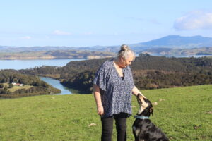 a woman standing on top of a hill overlooking the water with her dog looking up at her