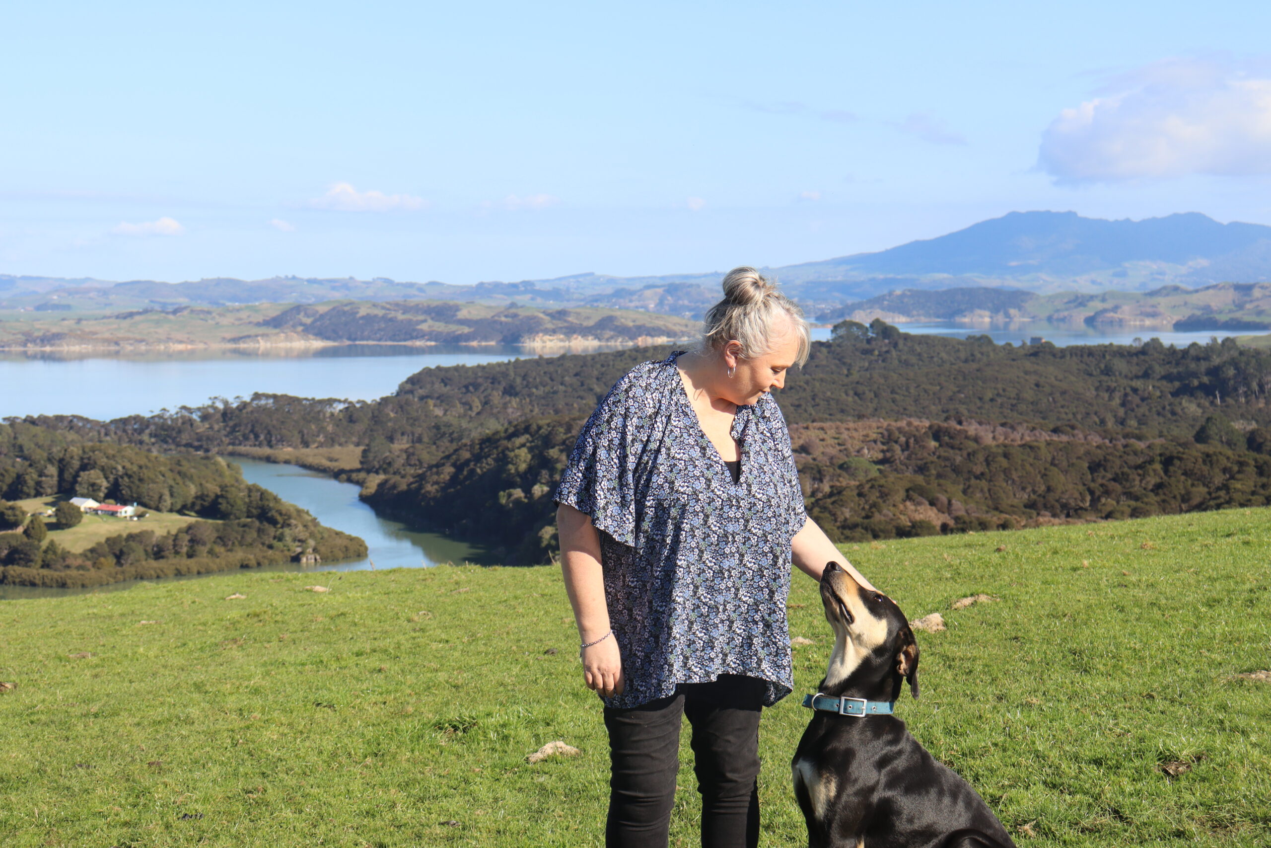 a woman standing on top of a hill overlooking the water with her dog looking up at her