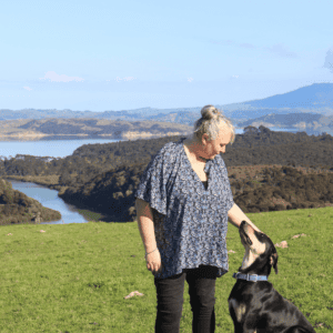 stacey and trix the dog sitting on a hill with a blue sky and harbor view of the water and rolling hills