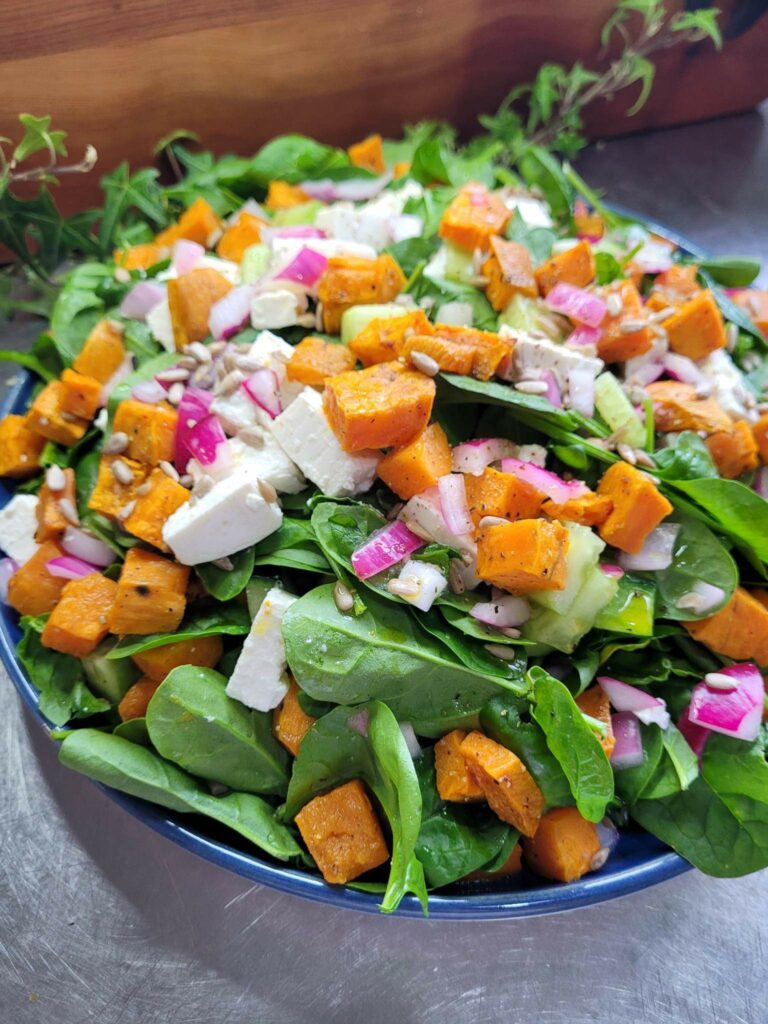 roasted sweet potato, spinach,red onion and feta salad in a blue bowl