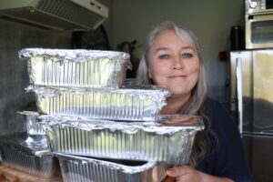 a woman holding tin foil trays with freezer meals