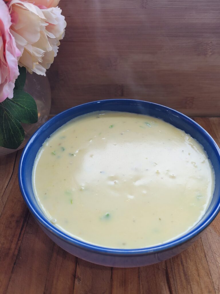 A steamy bowl of creamy chicken soup on a wooden board