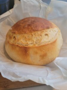 A round loaf of no-knead bread on baking paper just out of the oven