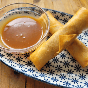 small bowl of caramel sauce with two apple pie spring rolls on a plate