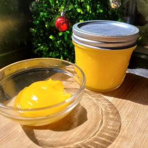 a jar of yellow lemon curd and a small bowl of lemon curd sitting on a wooden board