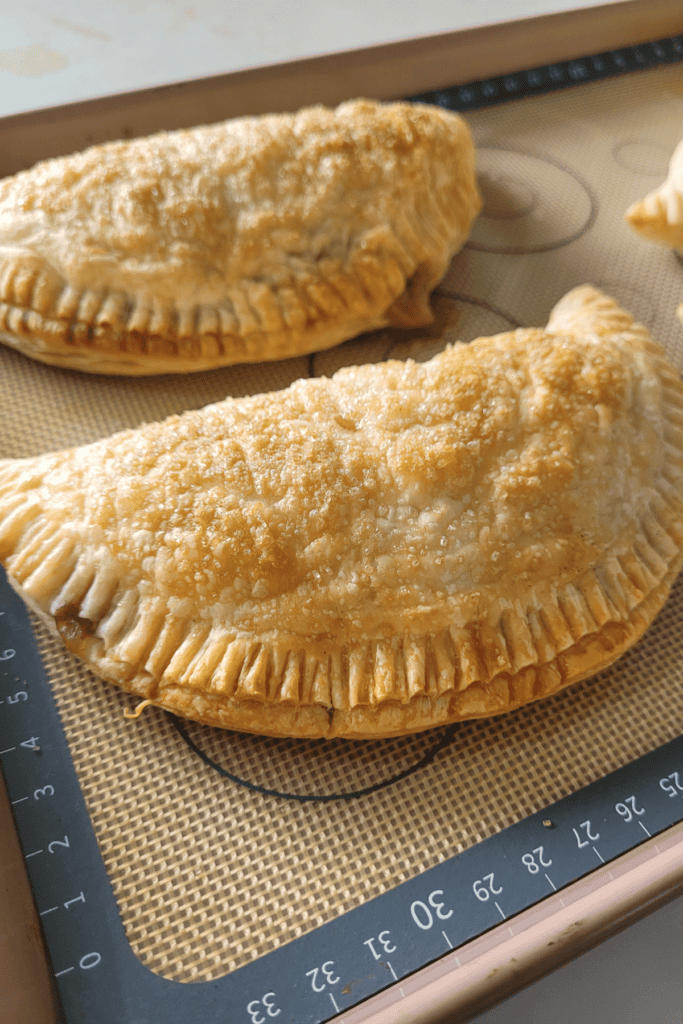 Golden semi circle of puff pastry filled with apple pie filling. The edges are crimped with a folk