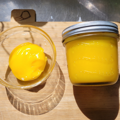 a jar and small bowl of lemon curd sitting on a wooden board