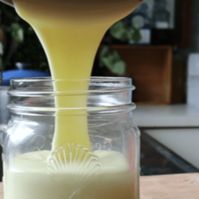 sweetened condensed milk being poured into a glass jar on a wooden board