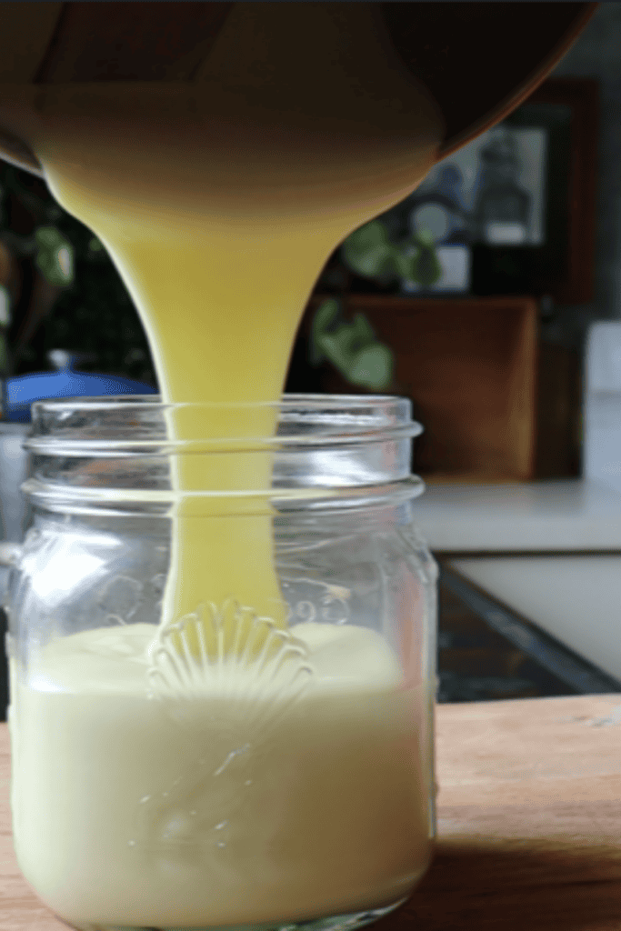 sweetened condensed milk being poured into a glass jar on a wooden board