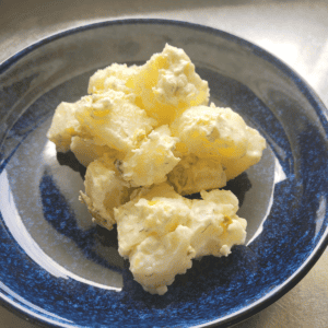 a blue bowl with creamy potato salad in the middle of the bowl. Sitting on a wooden board