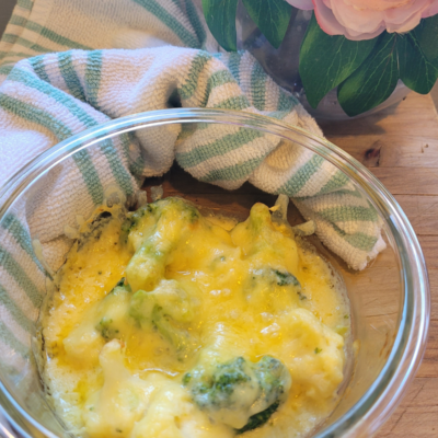 Easy Freezer Broccoli & Cauliflower Cheese Sauce in a bowl sitting on a wooden board it is topped with melted gooey cheese