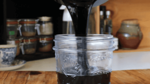Thick black balsamic glaze being poured into a glass jar