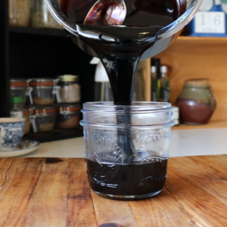 Thick black balsamic glaze being poured into a glass jar