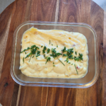 sweet corn relish dip in a rectangle glass container on a wooden board topped with chopped chives