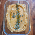 a glass container with sweet potato hummus it has pumpkin seeds as a garnish