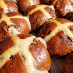 chocolate chip hot cross buns sitting on a wooden board with a white traditional cross