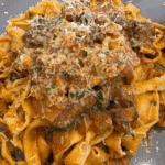a dish or homemade pasta with a slow-cooked lamb ragu with shaved cheese over the top