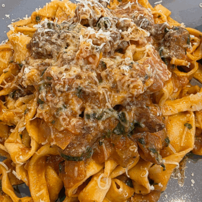 a dish or homemade pasta with a slow-cooked lamb ragu with shaved cheese over the top
