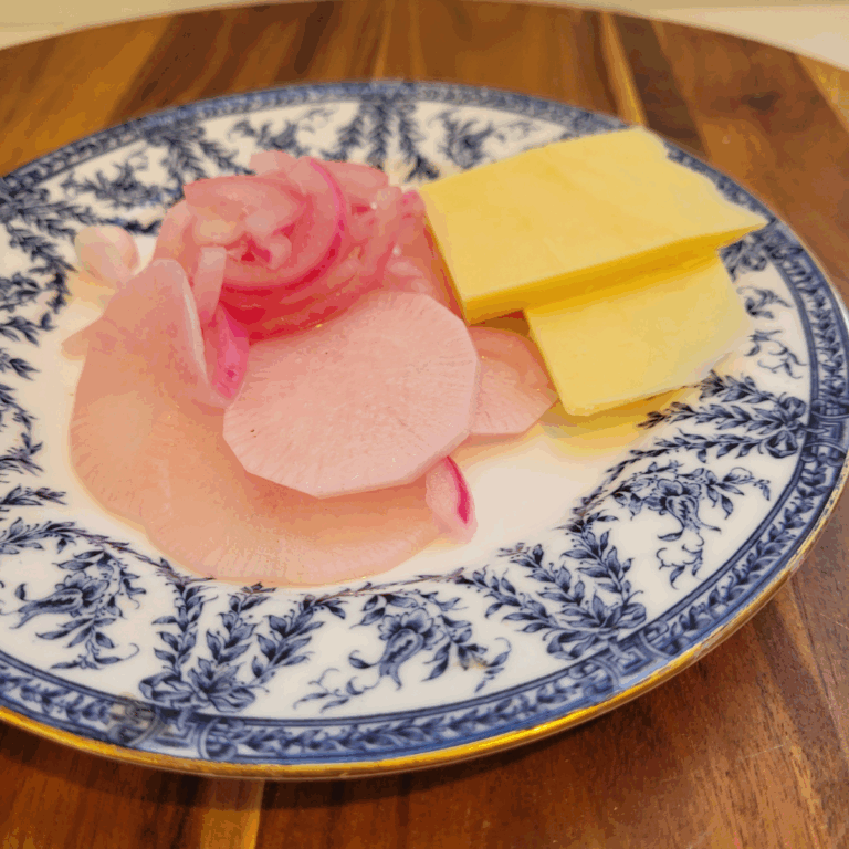 red onion and radish pickle on a blue plate. It has two slices of cheese as well.