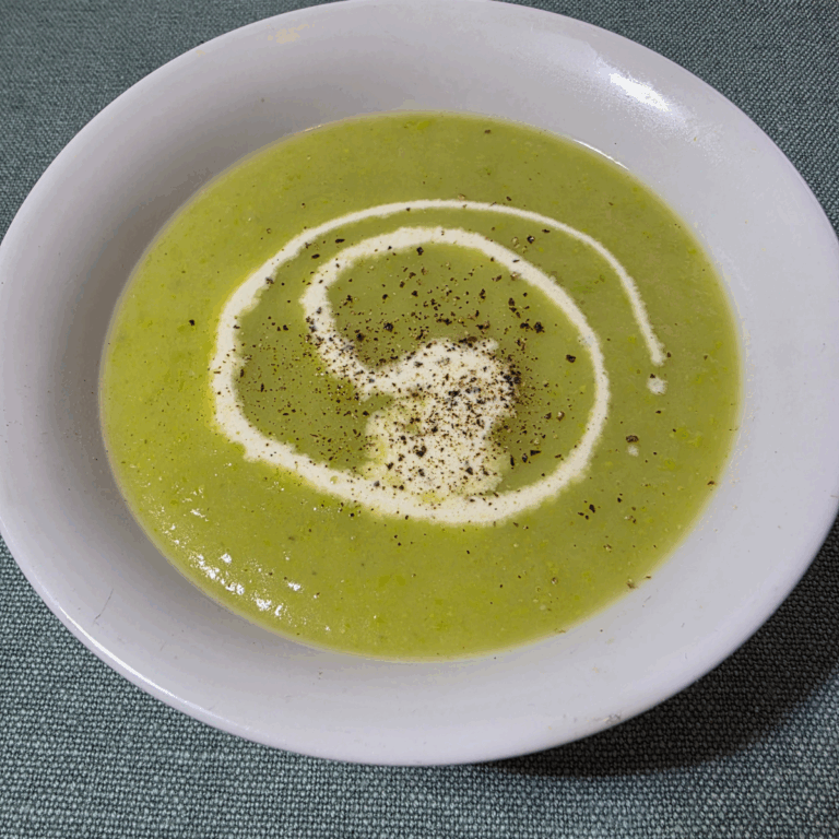 leek and potato soup in a white bowl with a swirl of cream and topped with cracked pepper. The soup is vibrant green