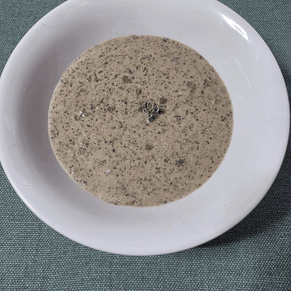 a bowl of creamy mushroom soup in a white bowl with some fresh thyme on top