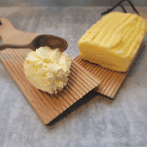 spreadable butter homemade sitting on a wooden butter pat board with homemade butter next to it