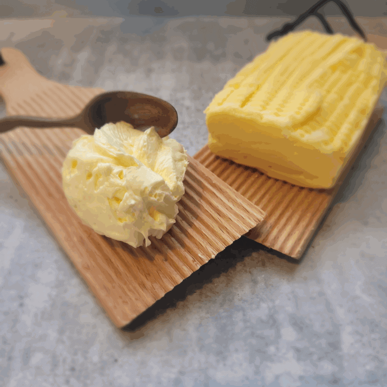 spreadable butter homemade sitting on a wooden butter pat board with homemade butter next to it
