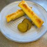 Golden cheeseburger spring rolls stacked on a rustic plate. With sweet and sour pickles