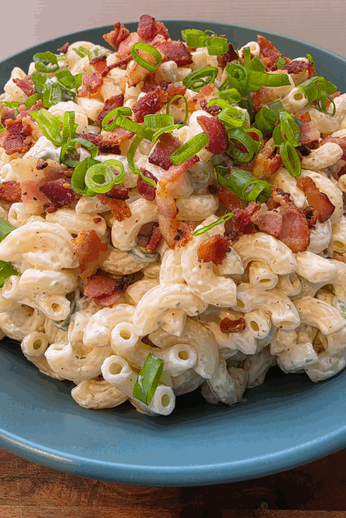 a bowl of loaded ranch macaroni salad topped with crispy bacon and spring onions