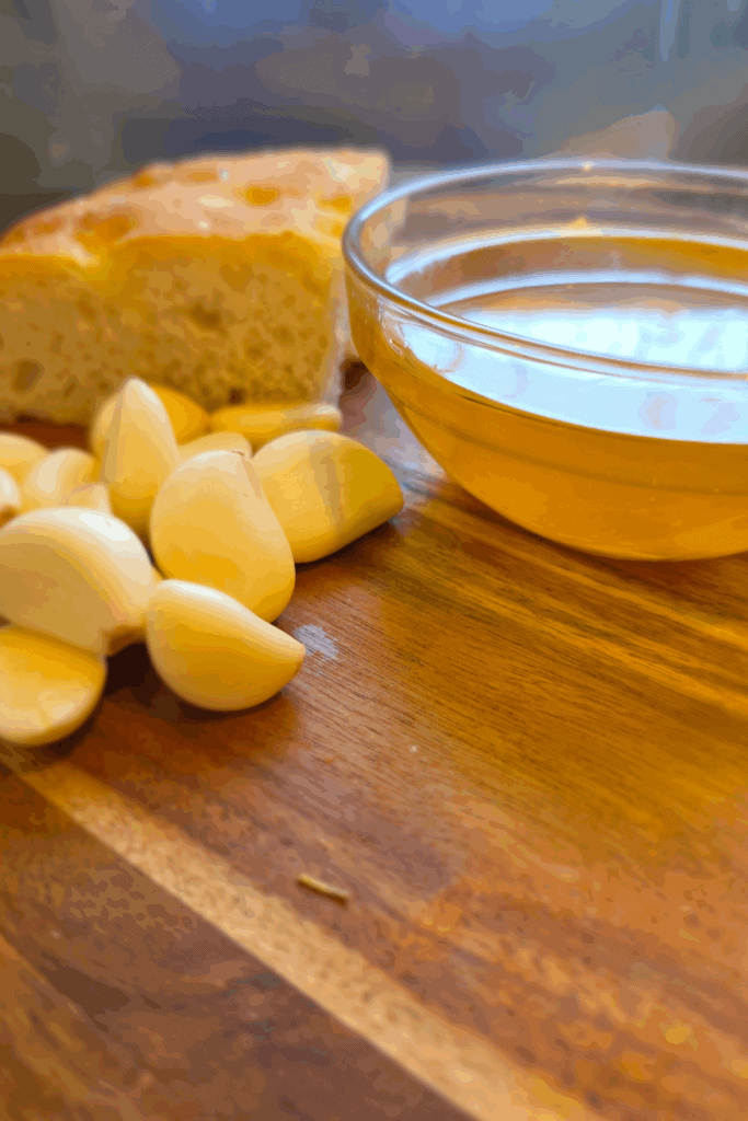 homemade garlic oil in a jar with fresh garlic cloves on a wooden board
