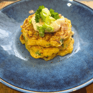 Golden homemade corn fritters stacked on a blue plate with sour cream and spring onions on top