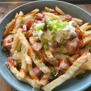 Plate of golden air-fried chips topped with melted cheese, diced ham, sour cream, and sliced spring onions, served warm and ready to enjoy.