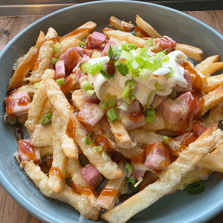 Plate of golden air-fried chips topped with melted cheese, diced ham, sour cream, and sliced spring onions, served warm and ready to enjoy.