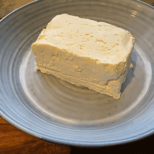 A blue plate with a rectangular cube of homemade cream cheese