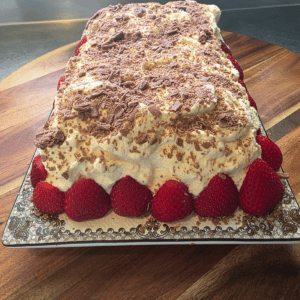 “Chocolate cookie log topped with chocolate flake and surrounded by fresh strawberries on a serving board.”