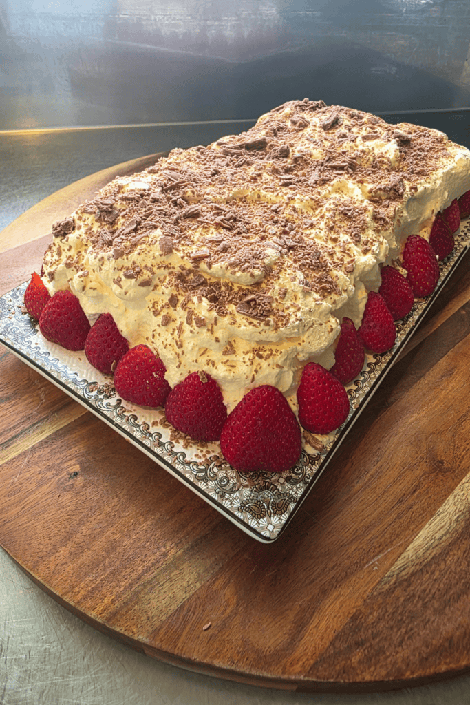 “Chocolate cookie log topped with chocolate flake and surrounded by fresh strawberries on a serving board.”