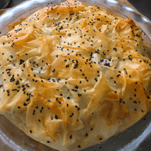“Golden crispy chicken and mushroom filo pie in a rustic dish, topped with flaky filo layers and black sesame seeds.”