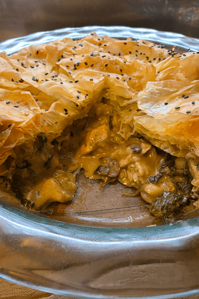 “Golden crispy chicken and mushroom filo pie in a rustic dish, topped with flaky filo layers and black sesame seeds.”