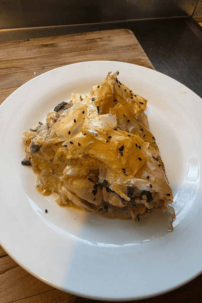 “Golden crispy chicken and mushroom filo pie in a rustic dish, topped with flaky filo layers and black sesame seeds.”