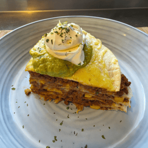 “Stacked Mexican-style tortilla bake layered with seasoned beef, cheese, and tortillas, sliced into wedges and topped with avocado and sour cream.”