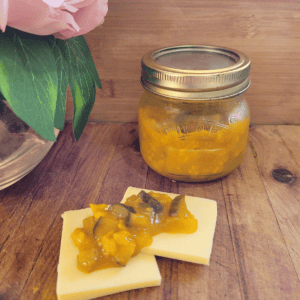 a jar of piccalilli with some slices of cheese and the preserve on top. sitting on a wooden board