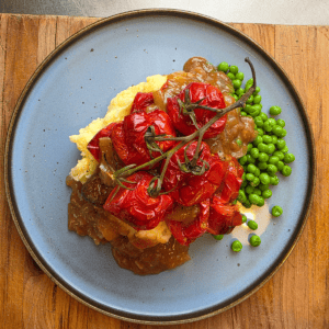 Plate of easy bangers and mash topped with rich onion gravy, roasted vine tomatoes & peas