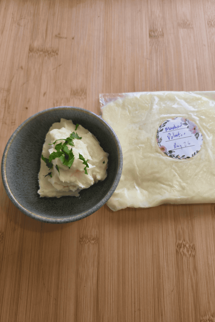 Leftover mashed potato frozen flat in a labelled freezer bag beside a bowl of creamy mashed potato